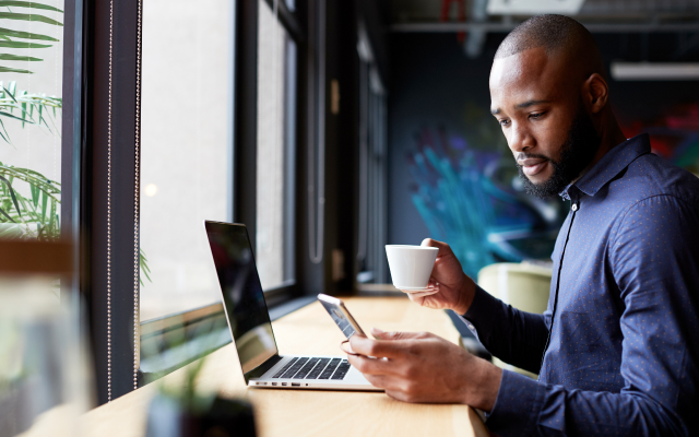 Man with coffee looking at mobile and laptop