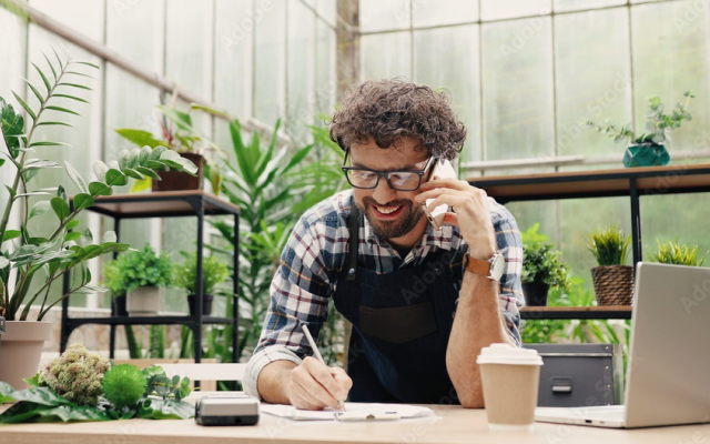 Happy man looking at laptop surrounded by plants. 