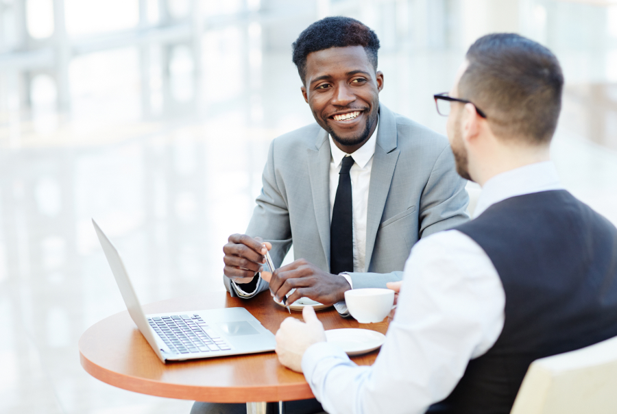 two men talking in front of a laptop screen