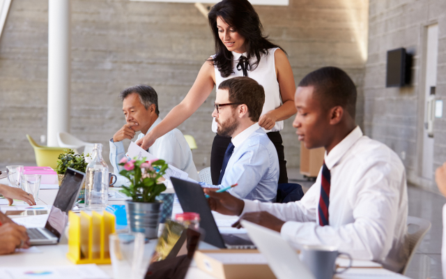 woman supervising group of three men at desktop computer