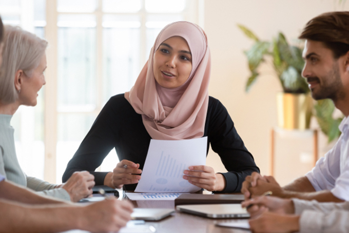 woman wearing headscarf talking to people at table