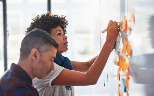 Man and woman putting post-it notes on a white board