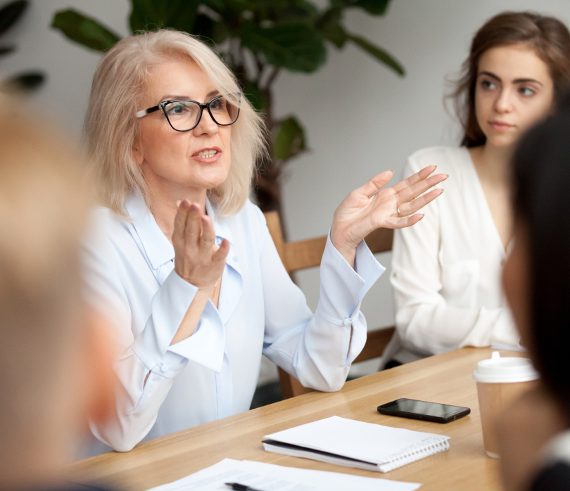 woman sitting at desk gesturing to other people