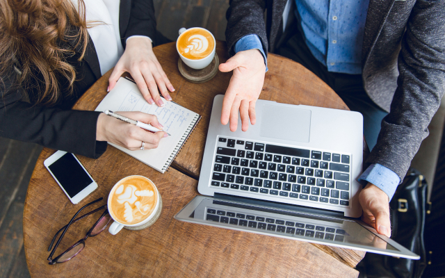 View from top of people sitting at a table with laptop and note book