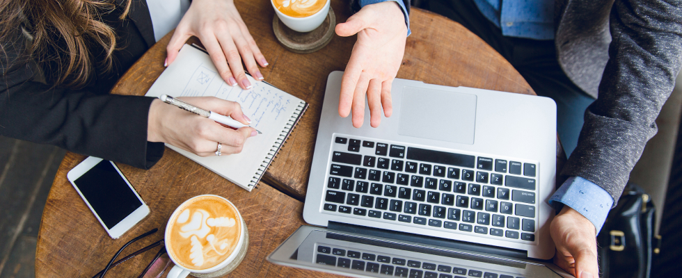 Bird's-eye view of people writing on notepad and using laptop