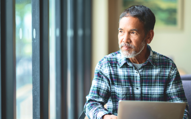 Man sitting at laptop looking out of window