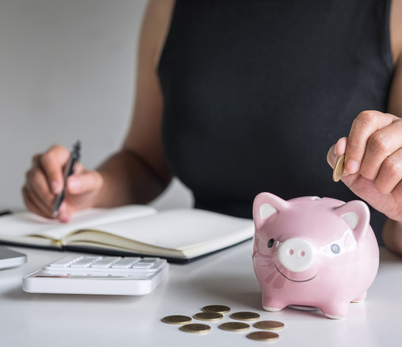 Person writing on notepad with piggy bank