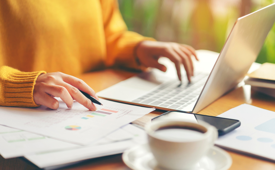 Person typing on laptop with coffee and paperwork