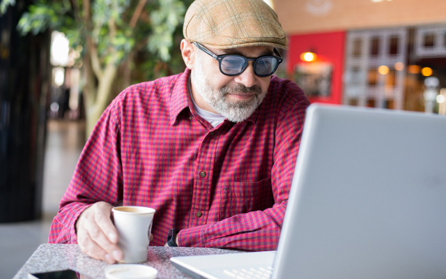 Older man in a coffe shop, looking at laptop screen