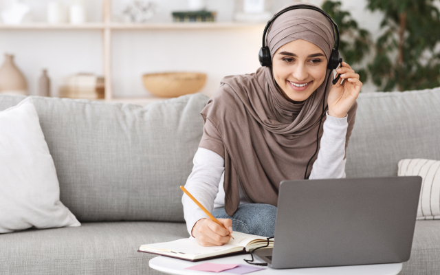 Woman with headscarf, with headset on looking at laptop