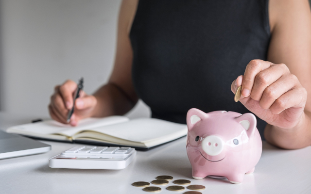 Person writing in notepad with piggy bank