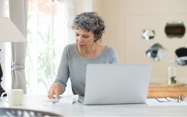 Older woman at table, looking at laptop