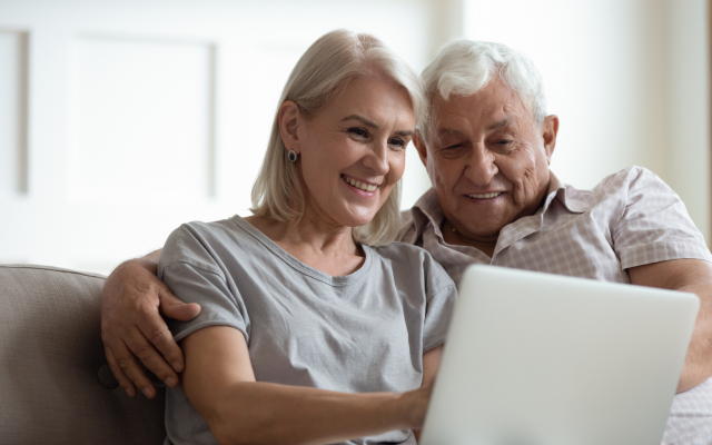 Middle aged man and woman sitting on sofa, looking at laptop